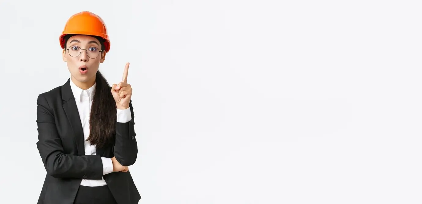 Eine kreative, intelligente asiatische Bauingenieurin hat eine großartige Idee; sie steht mit Sicherheitshelm und Schutzkleidung, hebt den Zeigefinger, äußert einen Gedanken oder Vorschlag, hat eine Lösung gefunden und teilt ihren Plan vor weißem Hintergrund.